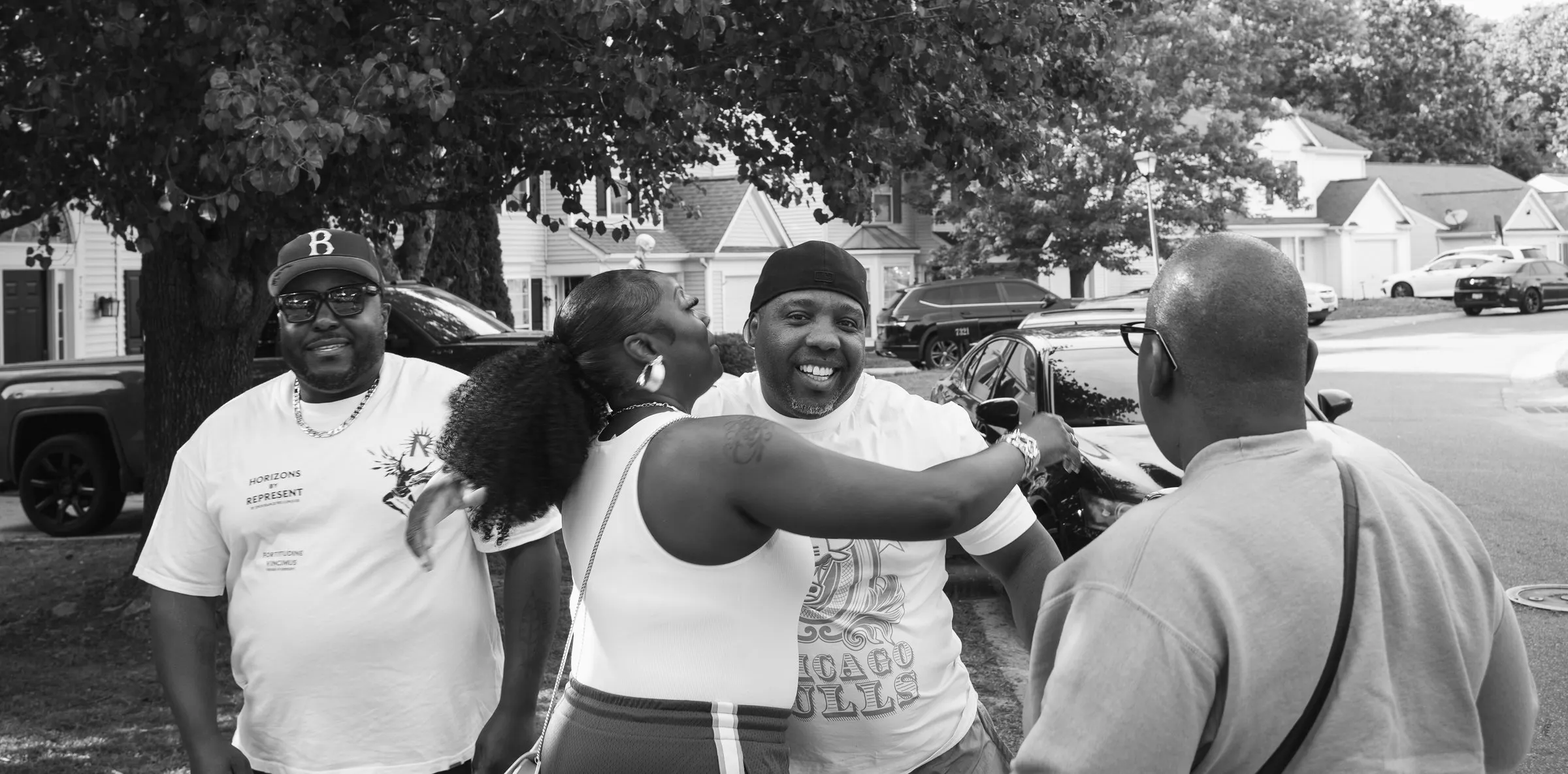 Black and white photograph of friends laughing and hugging as they arrive for the send-off