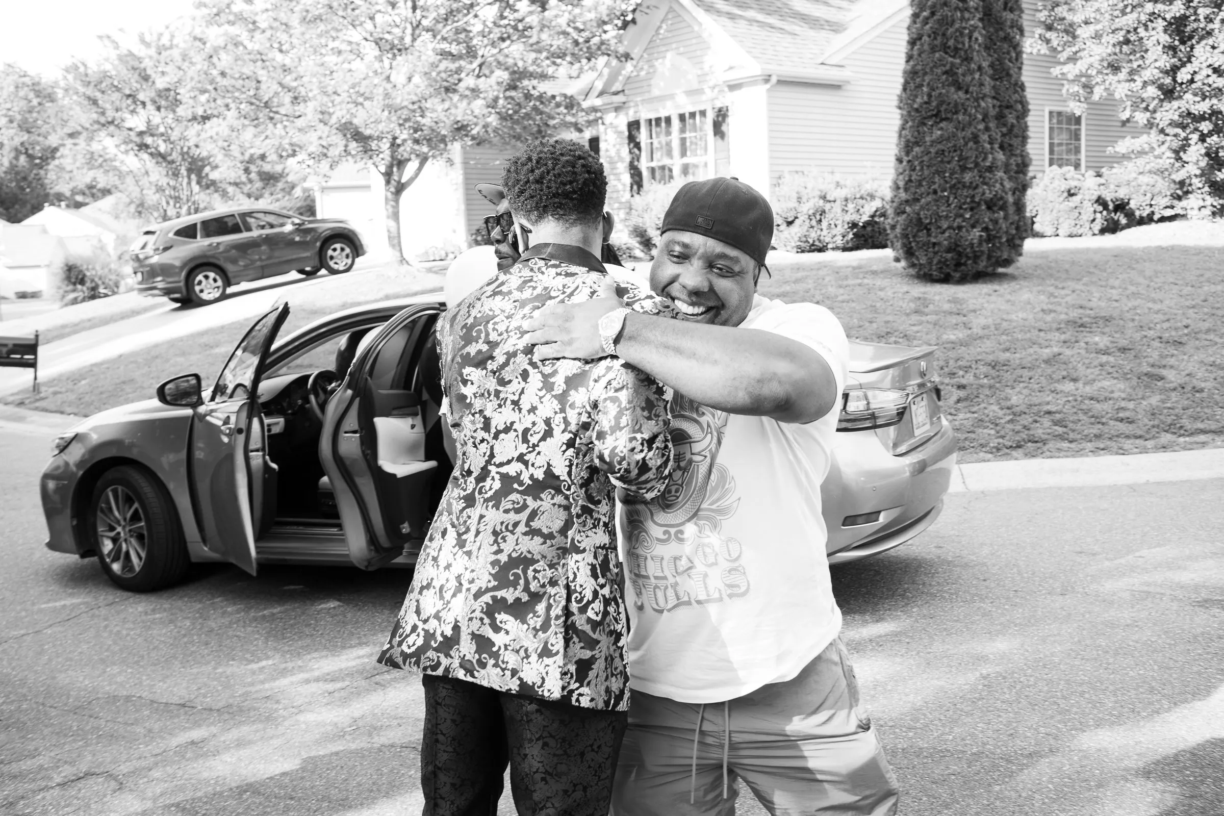 Black and white photograph of him hugging a guest beside an open car door
