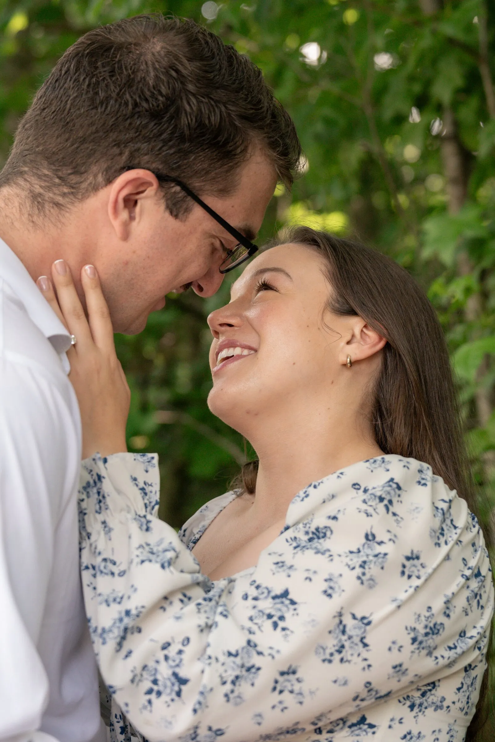 Kayla cradling Spencer's face and beaming up at him under green leaves