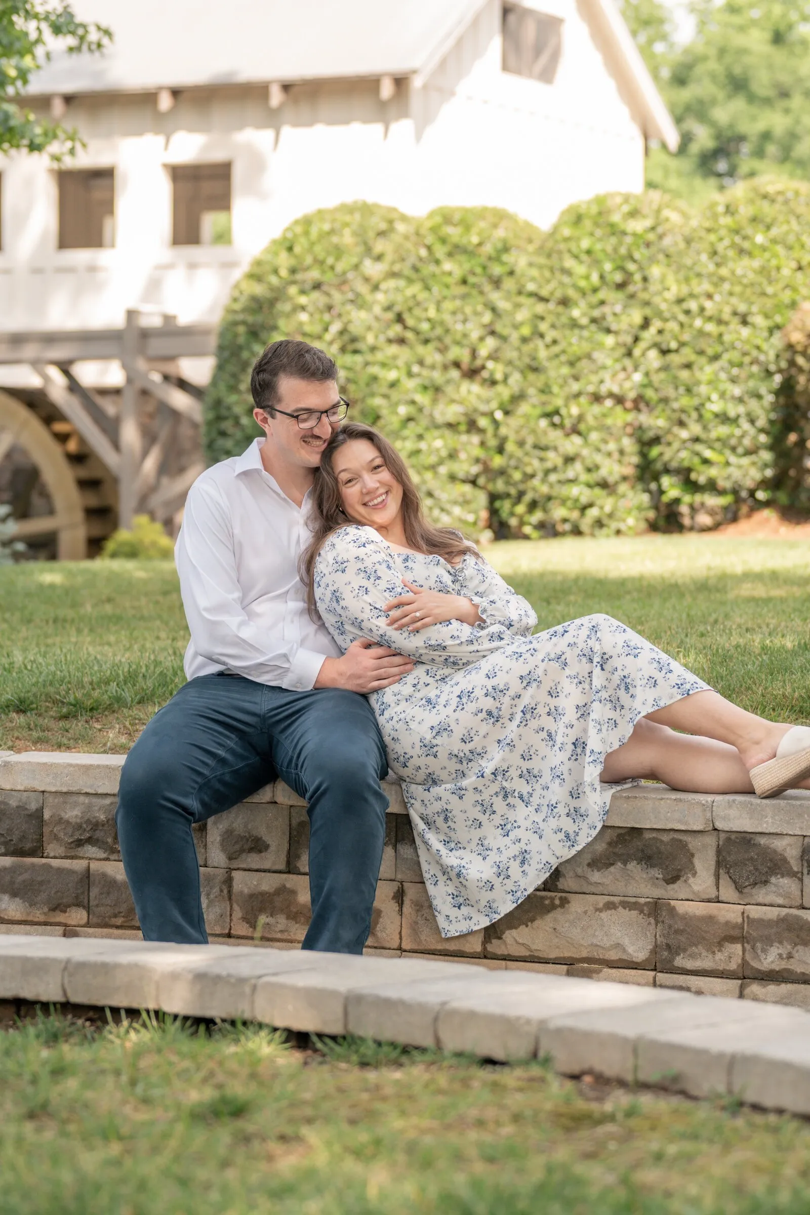 Spencer and Kayla sitting on a curved stone wall in front of the mill and its waterwheel