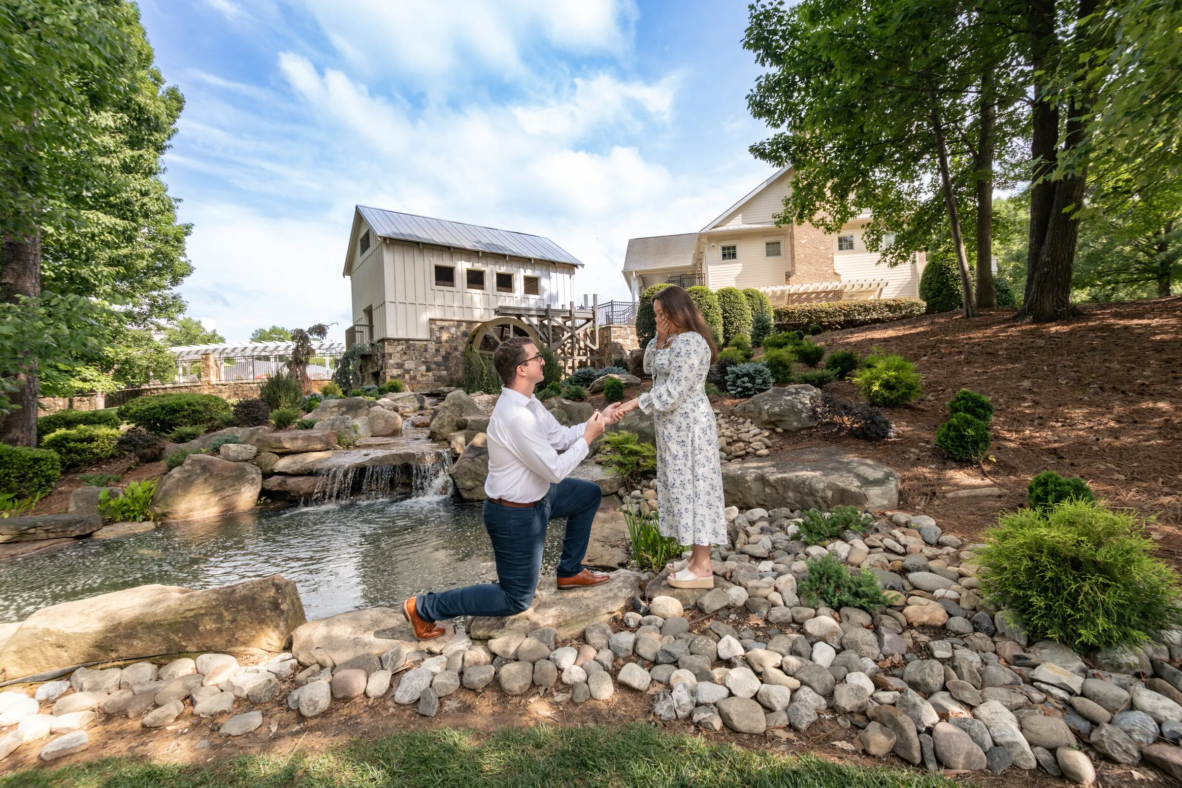 Spencer kneeling before Kayla beside the waterfall and pond at Millbridge