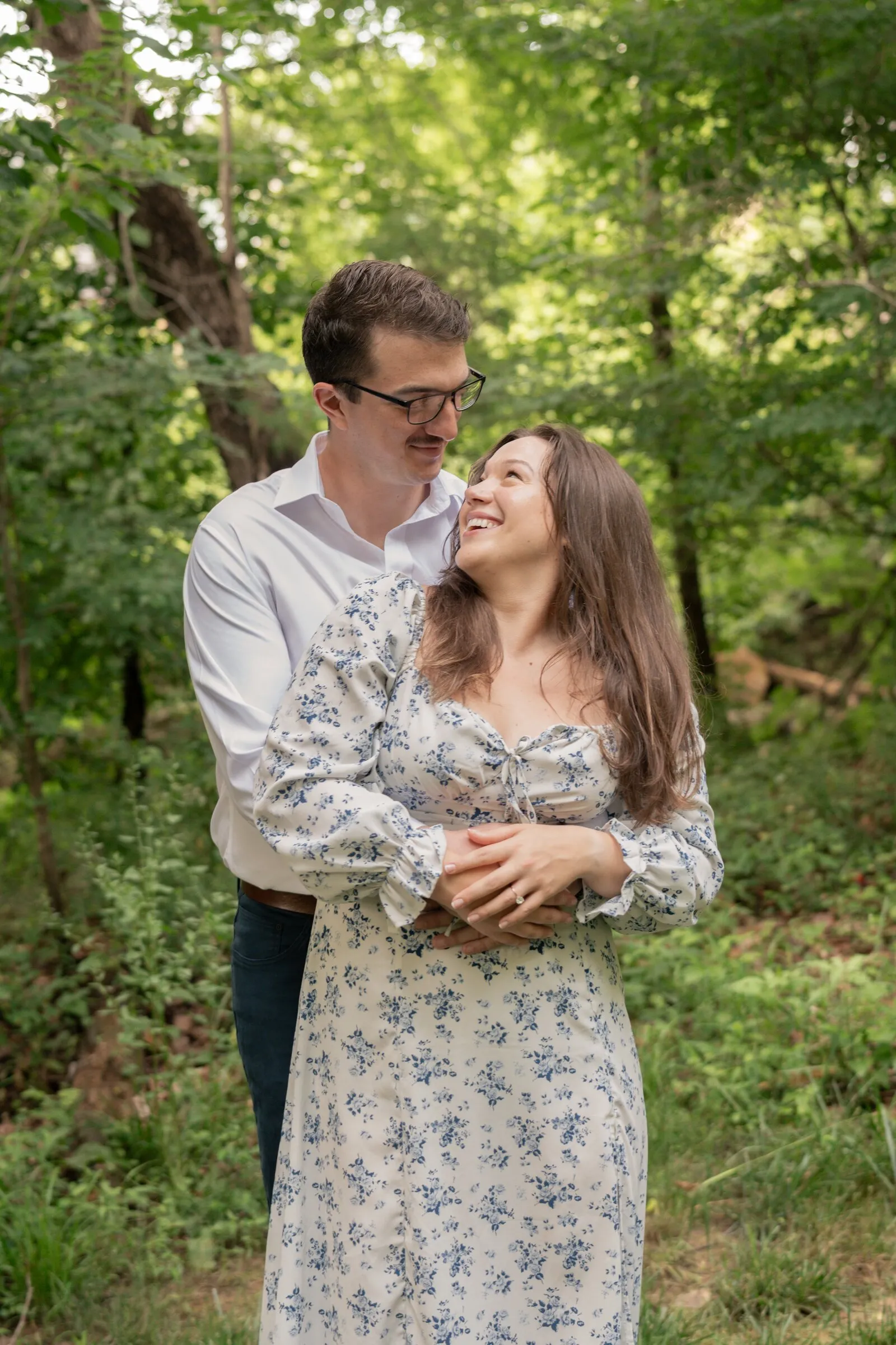 Spencer holding Kayla from behind in the woods as she looks up and smiles at him