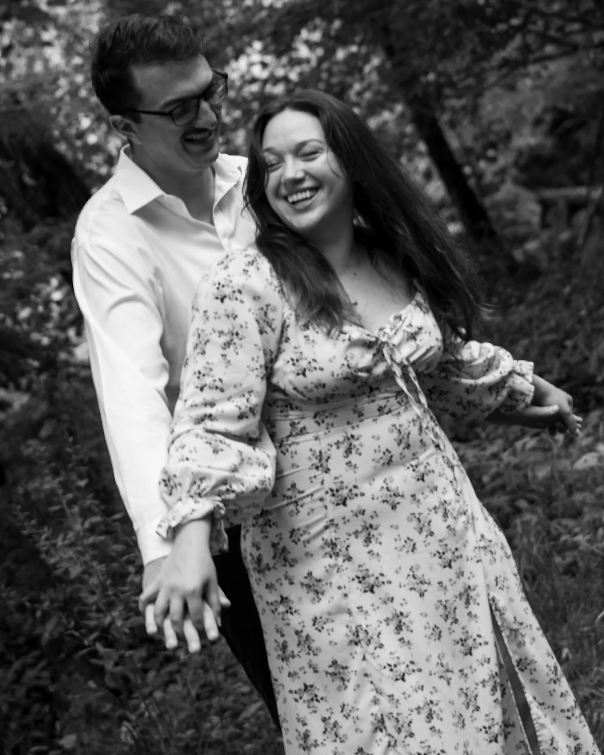 Black and white photograph of Kayla laughing as she twirls away from Spencer, hands still joined