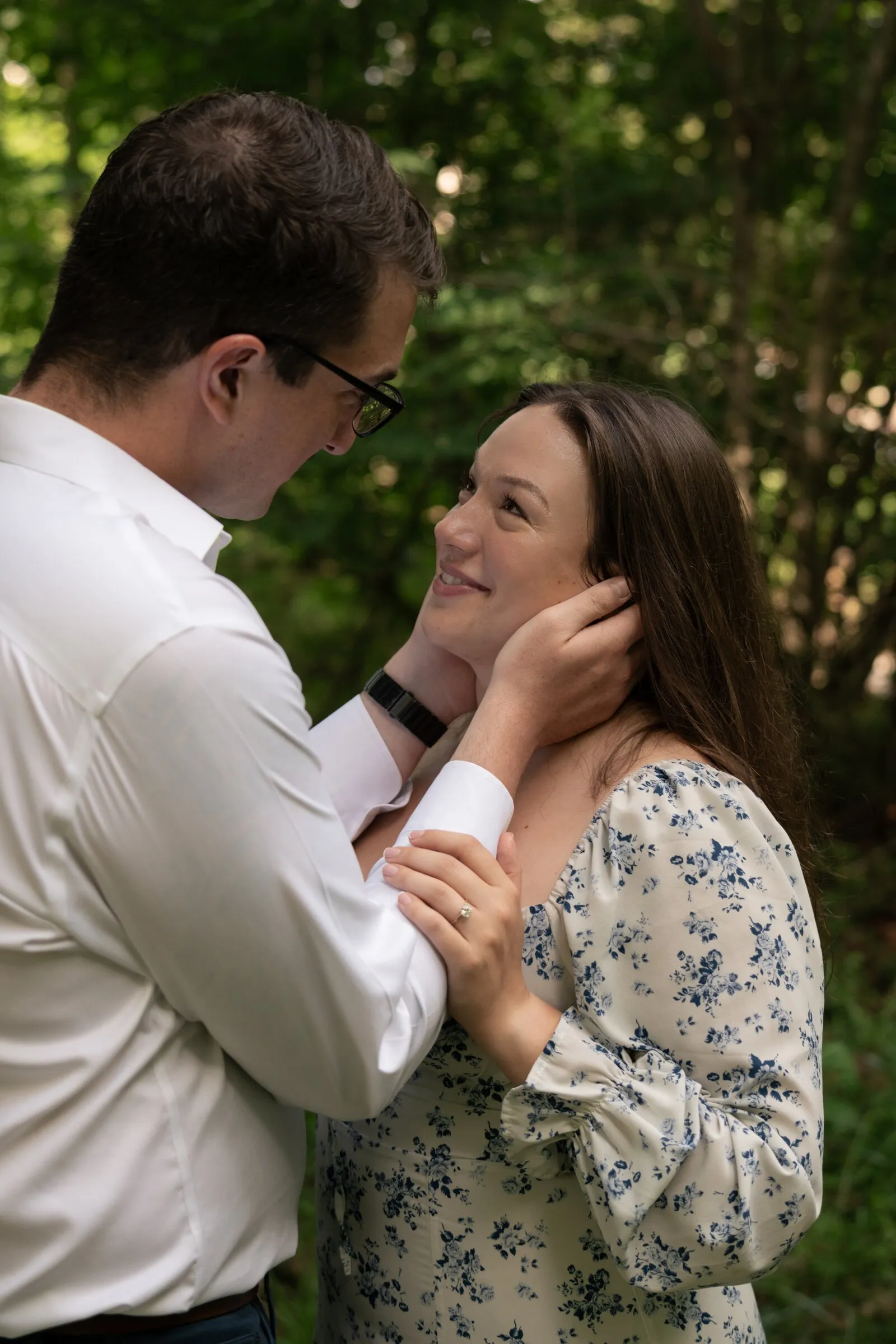 Spencer looking down at Kayla as she holds his wrists, both framed by the woods