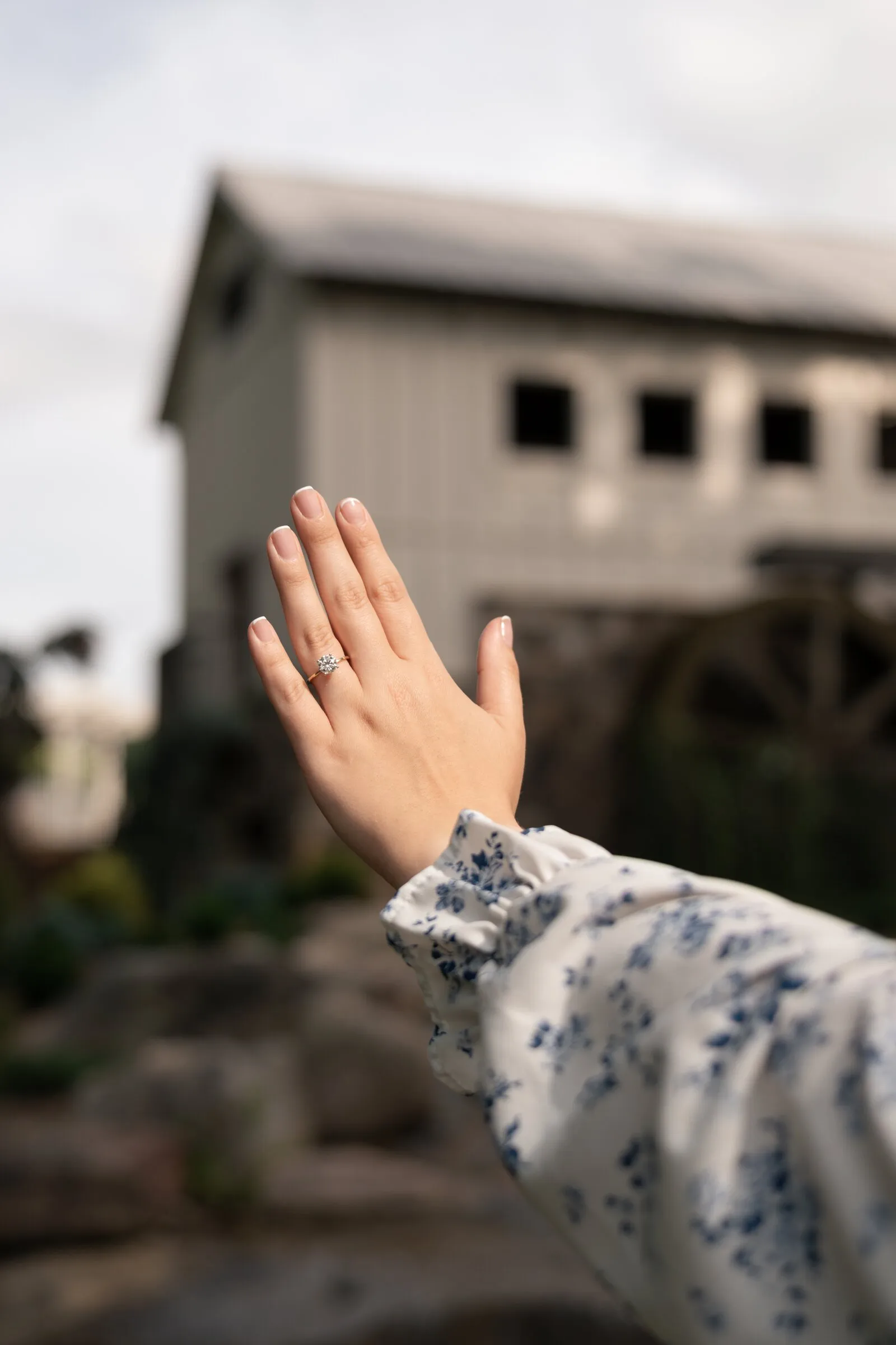 Kayla holding up her ring hand toward the Millbridge mill house