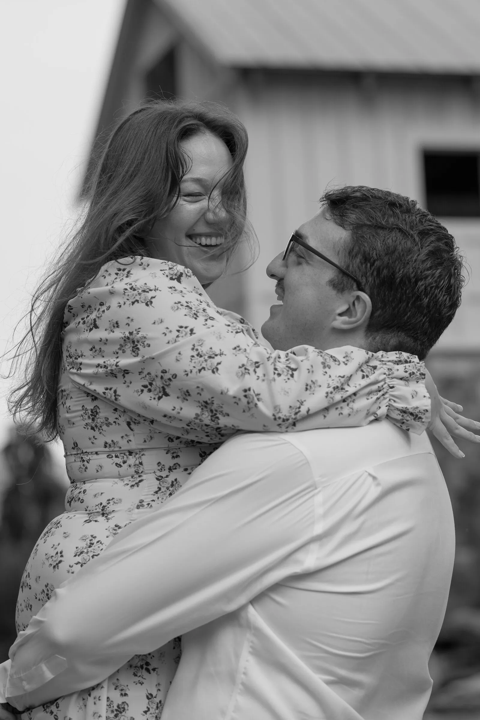 Black and white photograph of Kayla laughing with her arms around Spencer as he lifts her