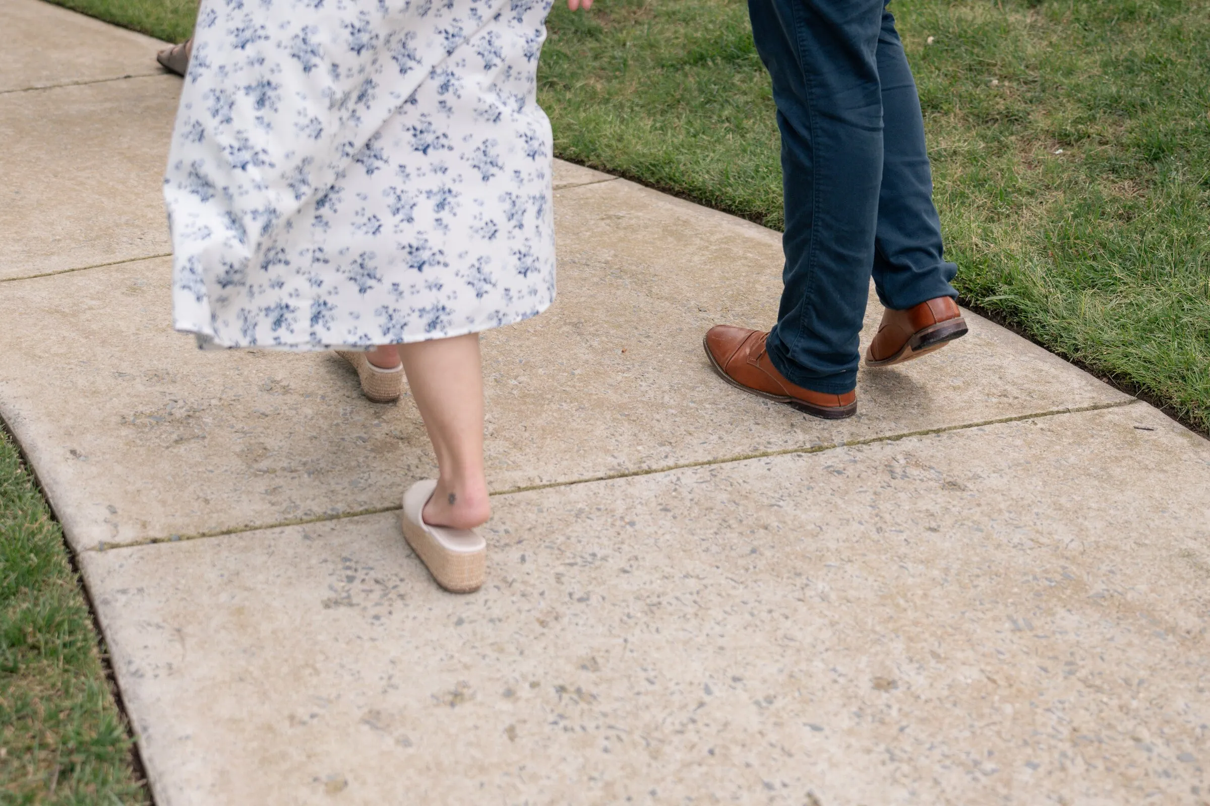 Detail of Kayla's floral hem and Spencer's brown shoes as they walk along the sidewalk