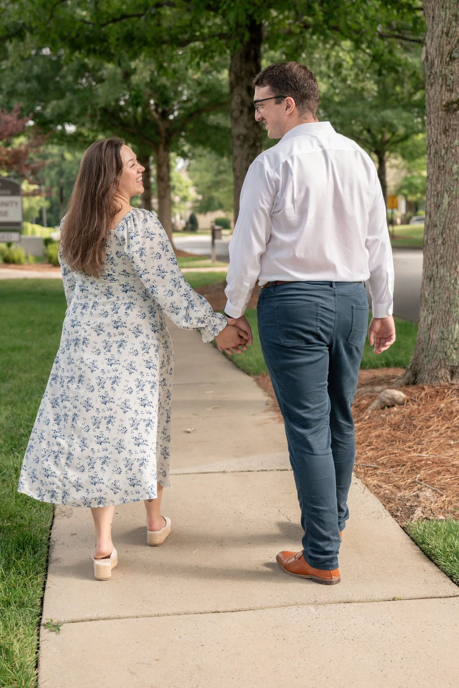 Spencer and Kayla walking hand in hand down a tree-lined sidewalk in Millbridge