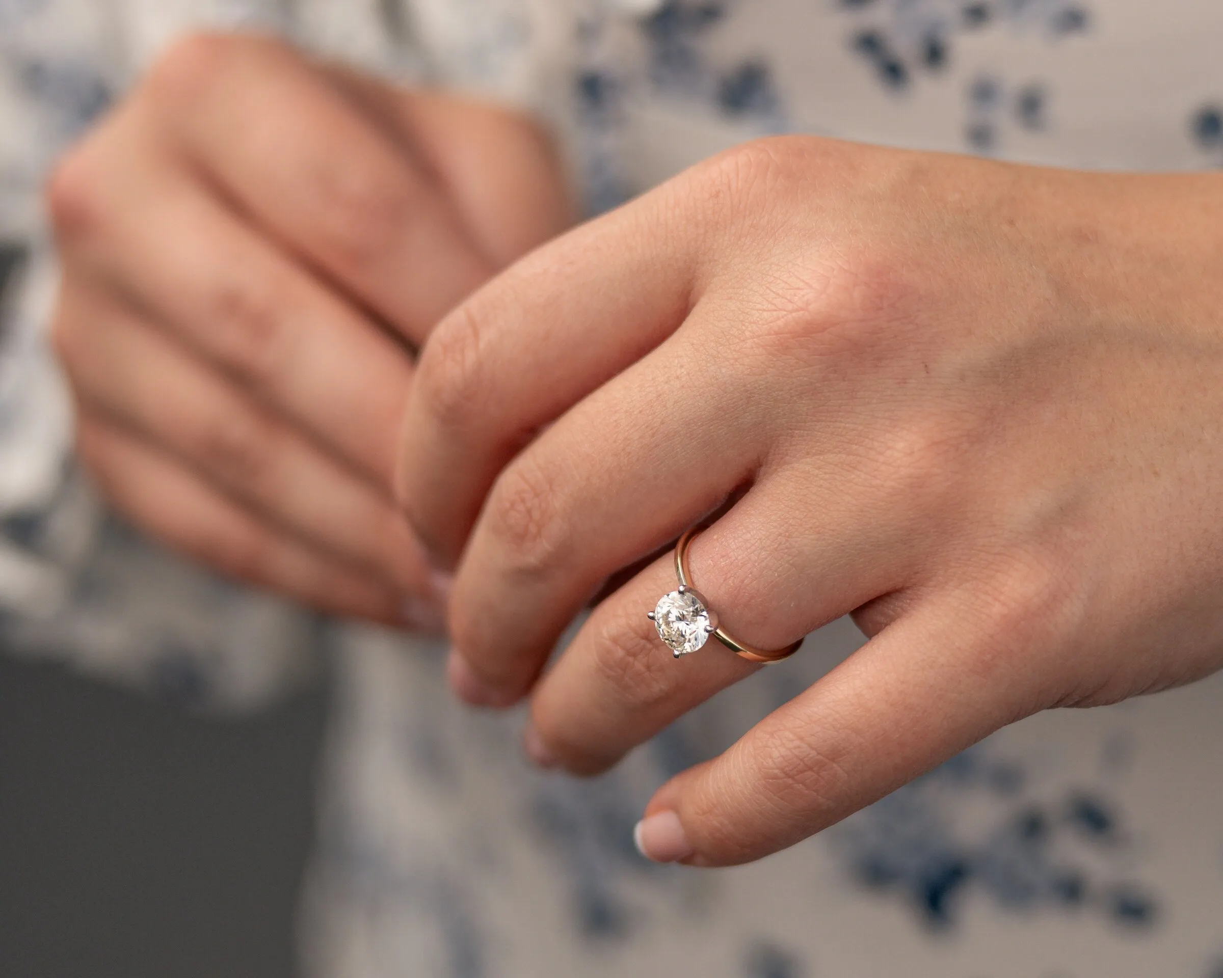 Close-up of Kayla's hand in Spencer's, her round solitaire set on a rose gold band