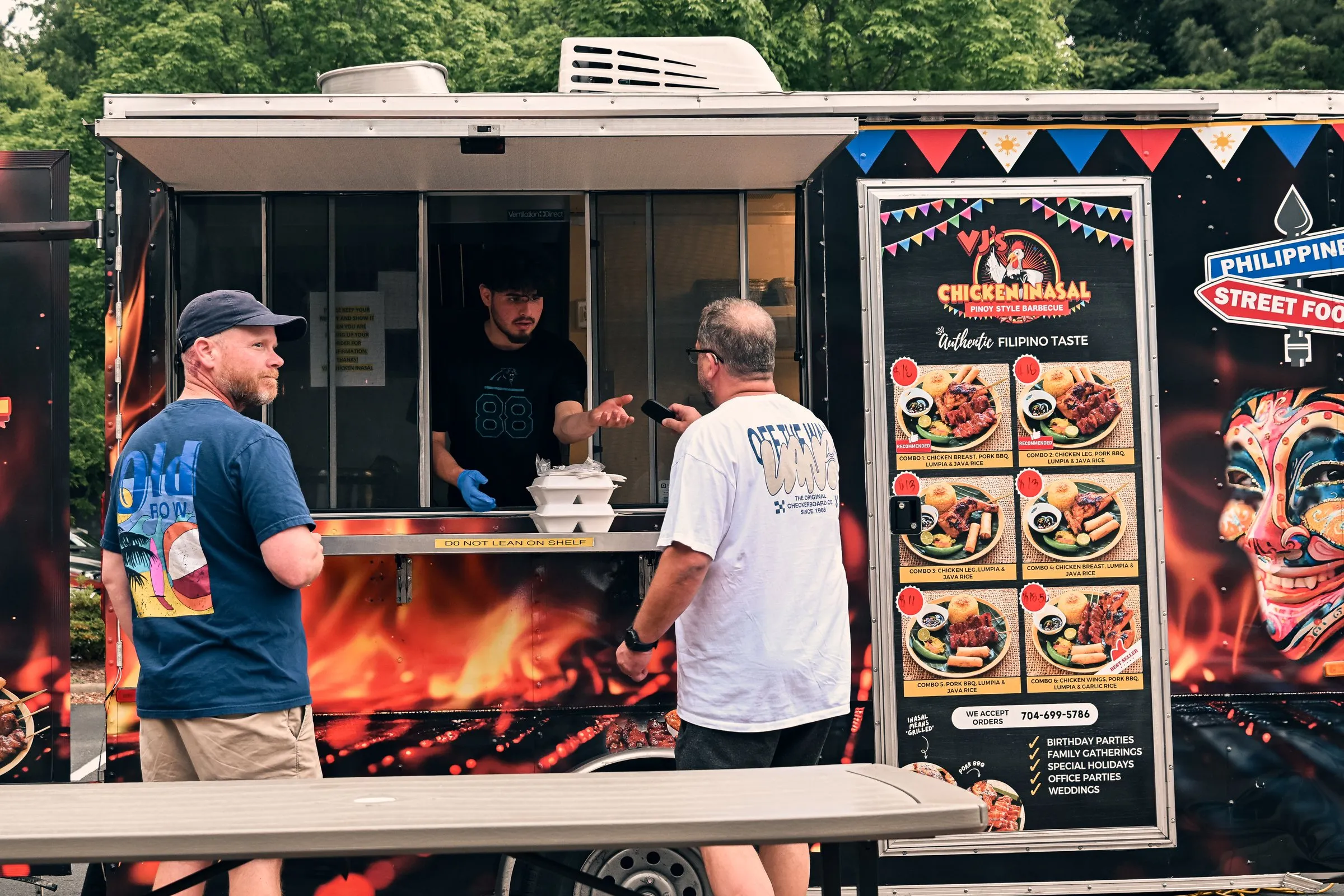 Customers at the food truck window beside its Philippine Street Food sign and menu board