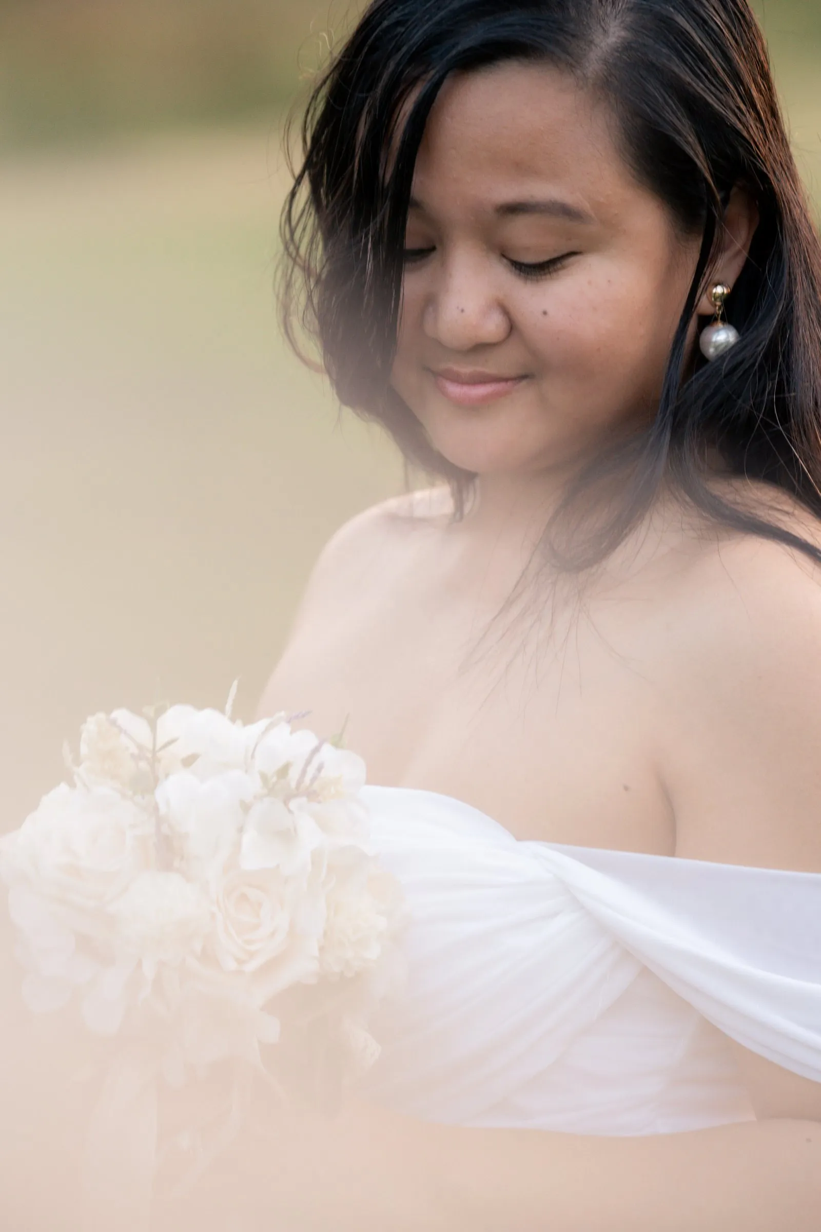 Winnie looking down and smiling over her bouquet in a soft, hazy evening light