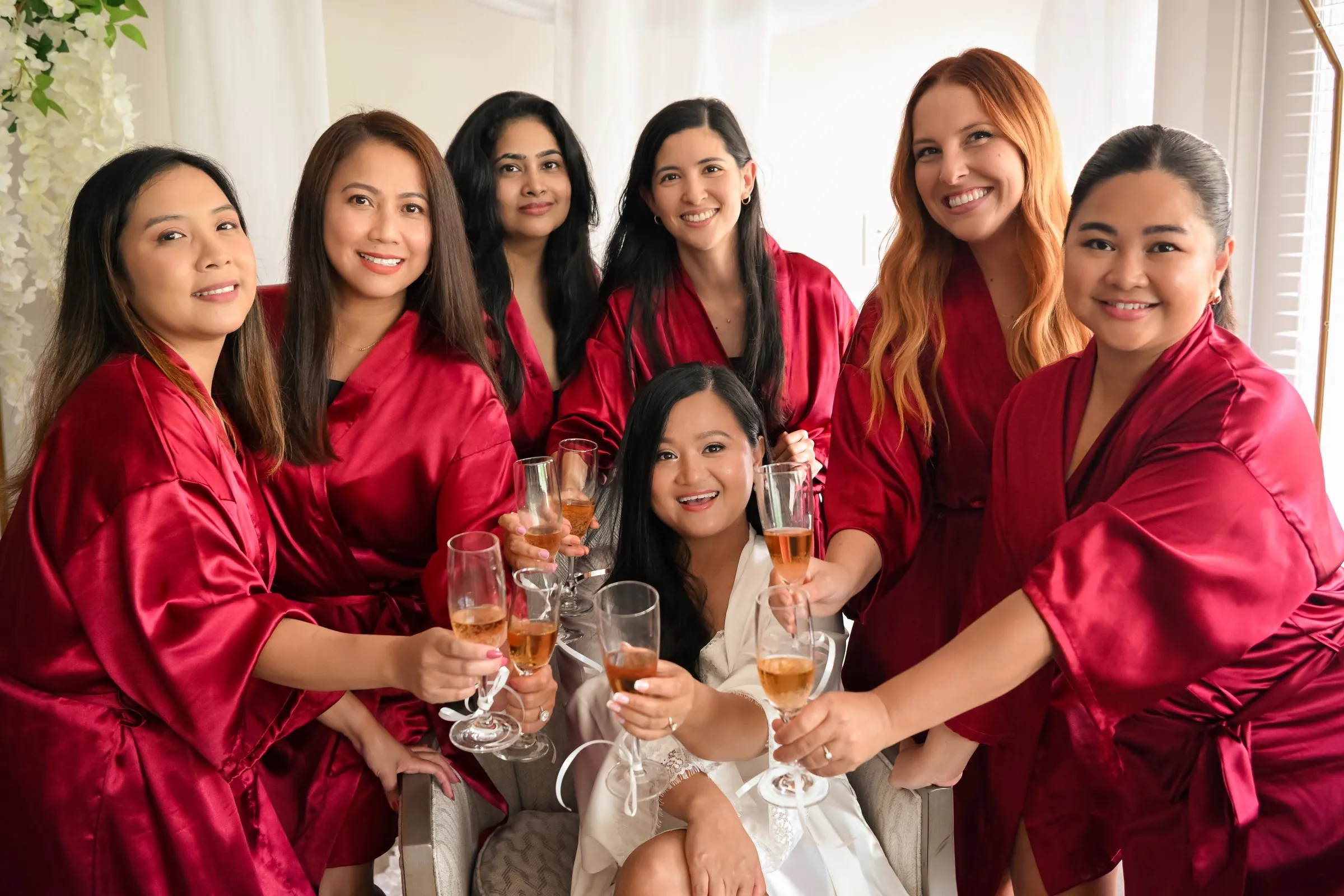 Bridesmaids in red robes leaning in to clink their champagne glasses with Winnie