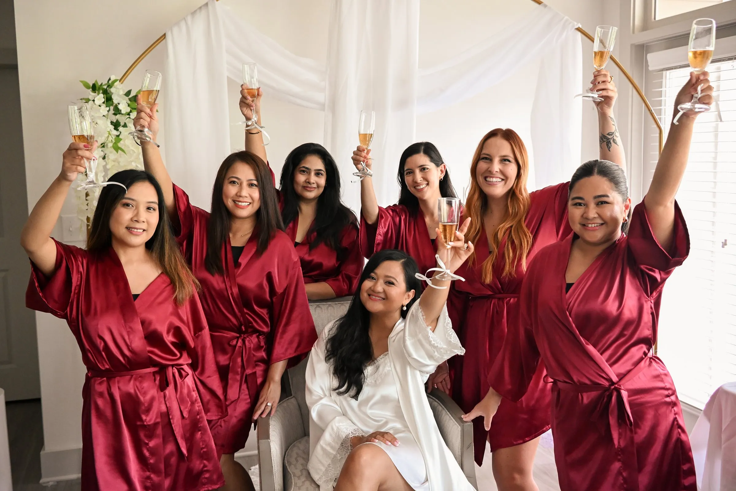 Winnie and her bridesmaids cheering with champagne raised overhead in the bright getting ready suite