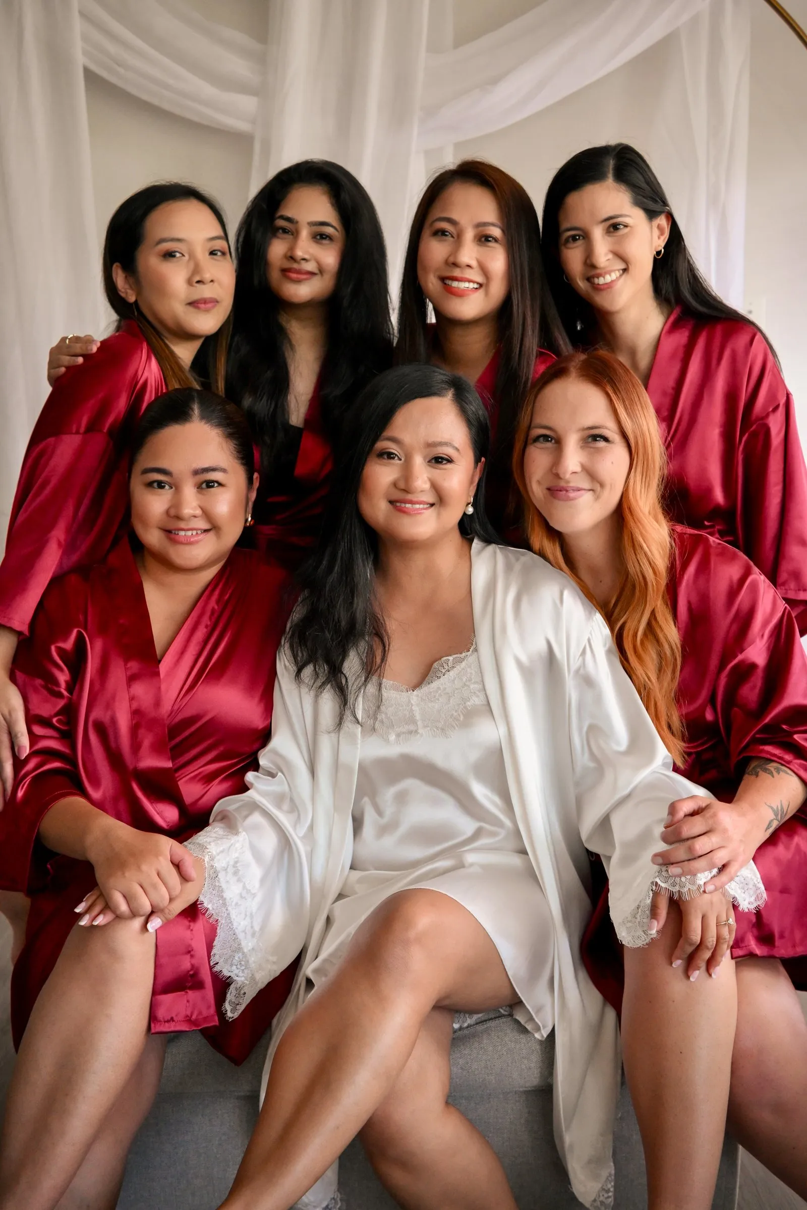 Winnie in a white satin robe among her bridesmaids in red satin robes on her wedding morning in Charlotte, NC