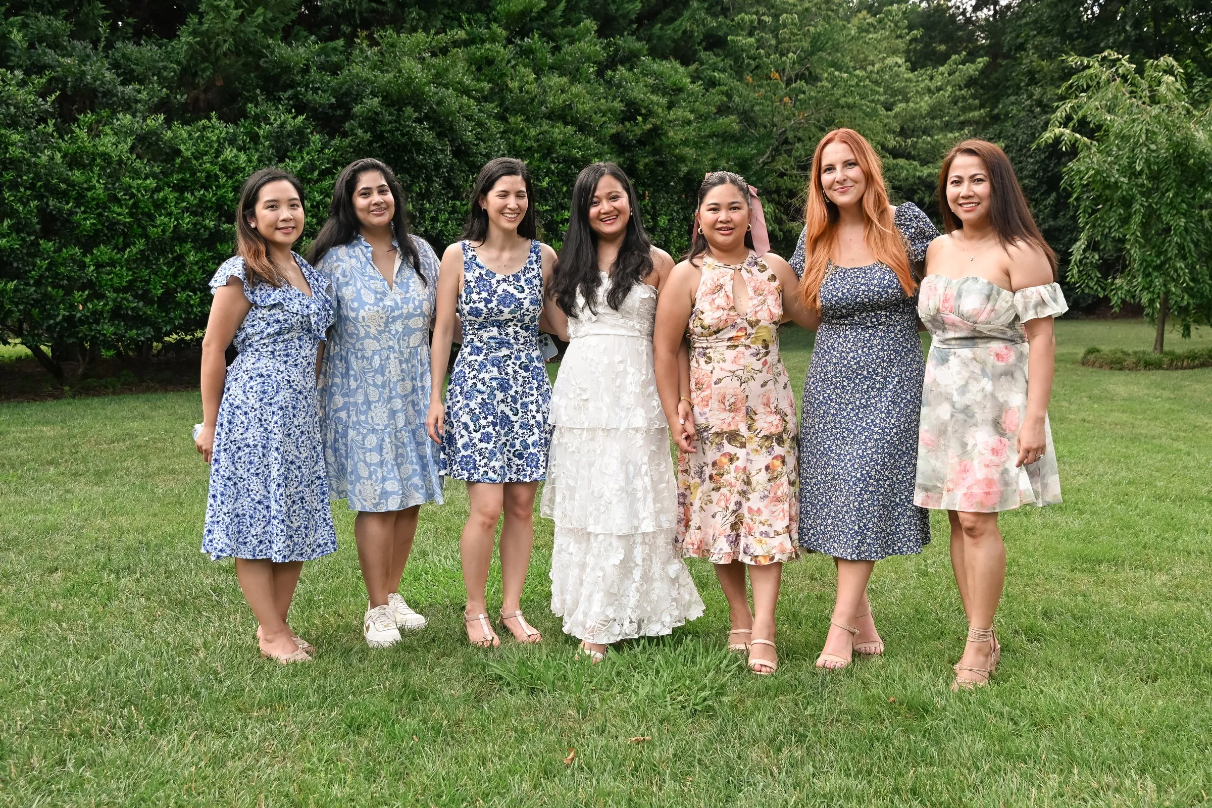 Winnie in white with six bridesmaids in blue and blush floral dresses on the lawn at Alexander Homestead in Charlotte