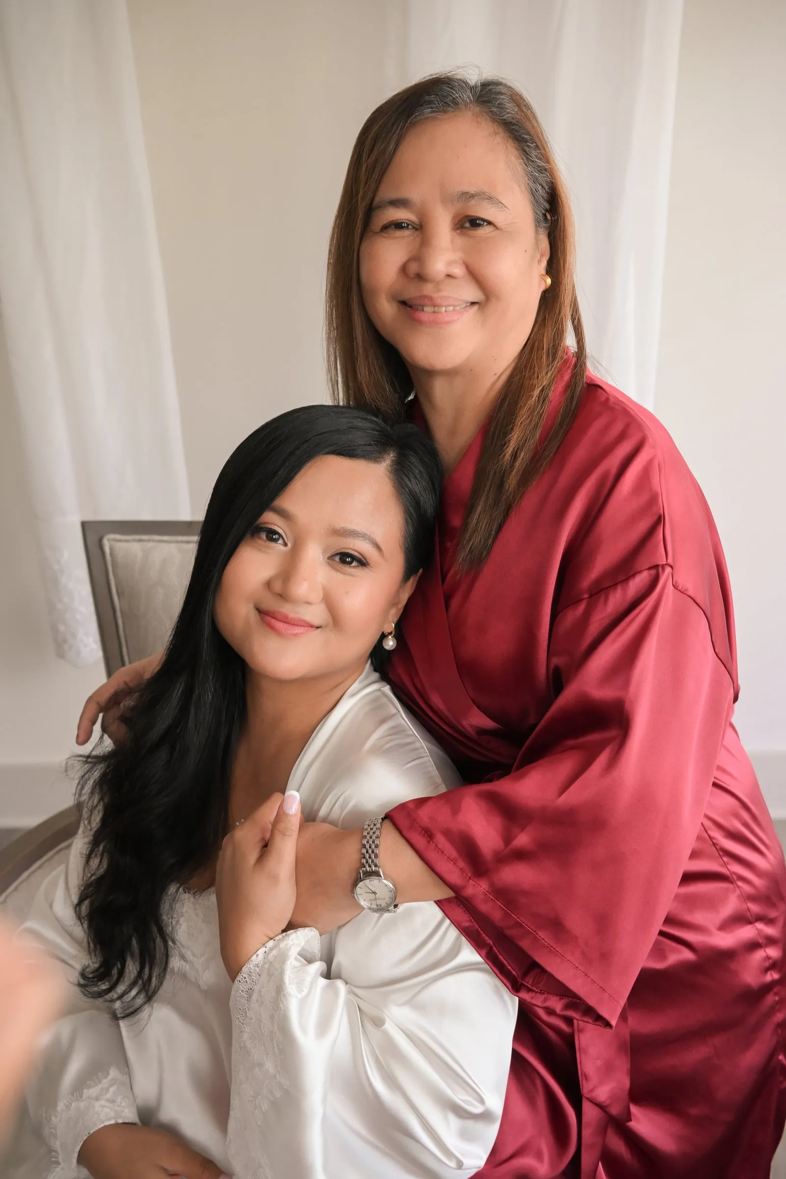 Winnie and her mom in a red satin robe embracing and smiling at the camera